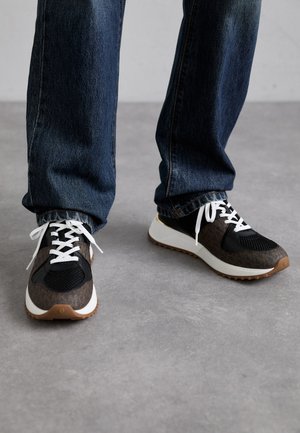 Black and brown athletic shoes with mesh and synthetic upper, white laces, and textured rubber sole, paired with blue denim jeans.