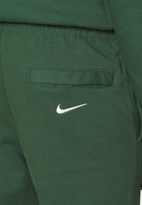 Gröna Nike-joggingbyxor med en mjuk textur, med en liten vit logga och en bakficka med horisontell öppning.