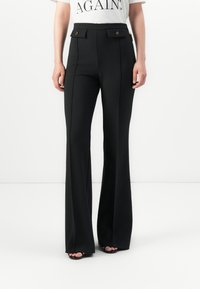 Black high-waist flare pants with front seams and buttoned flap details, worn with a white T-shirt and black open-toe shoes.
