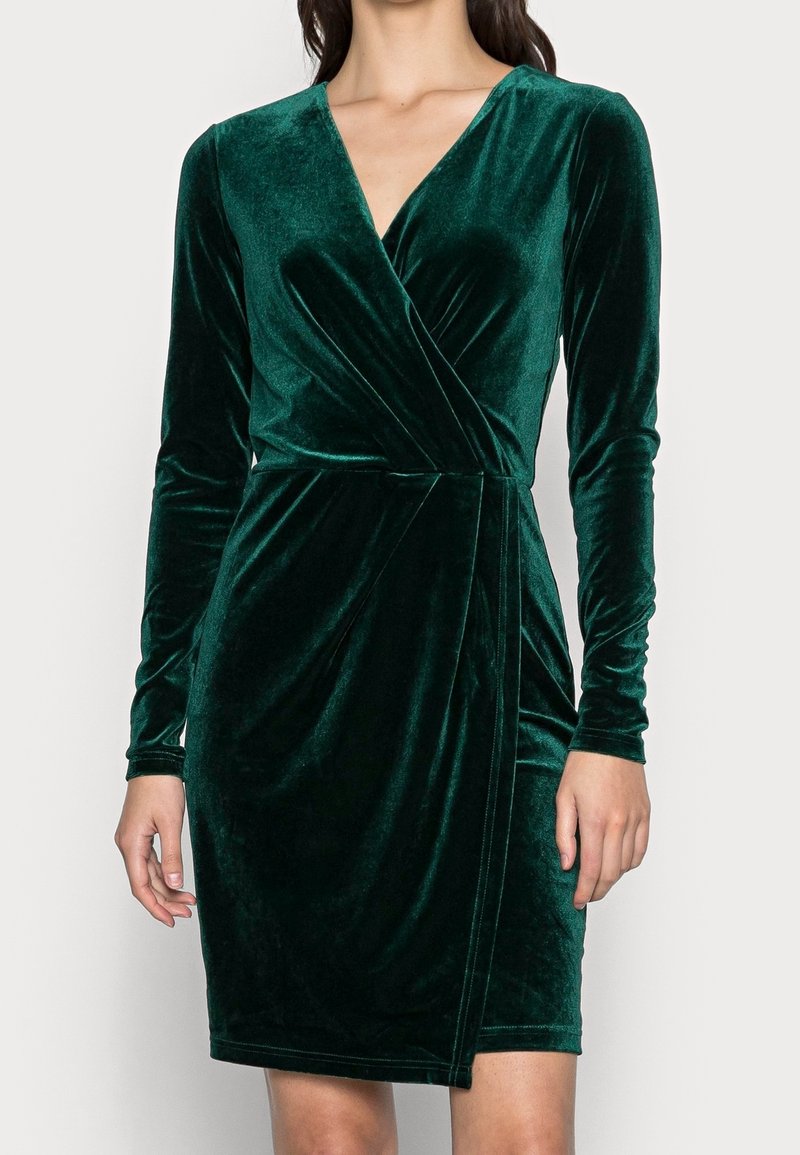 Robe verte en velours avec manches longues, design portefeuille et effet drapé. Dotée d'un décolleté en V profond et d'une silhouette ajustée. Texture lisse.