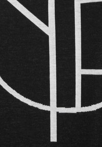 Svart tyg med ett stickat mönster som innehåller djärva, vita geometriska former, inklusive ett stort "Y" och en böjd linje, vilket skapar en slående kontrast.