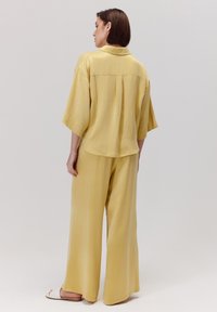 Żółta, oversize'owa koszula i szerokie spodnie, wykonane z miękkiego materiału, z krótkimi rękawami i delikatnym blaskiem, widziane z tyłu.