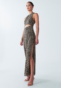 Haljina s leopard uzorkom s izrezima i bočnim prorezima, napravljena od glatkog materijala. Ima okrugli izrez i uski kroj, uparen s neutralnim potpeticama.