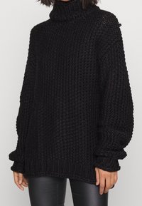 Schwarzer, übergroßer Strickpullover mit Stehkragen, strukturiertem, groben Gewebe, langen Ärmeln und geripptem Saum. Weiches Material mit lässiger Passform.