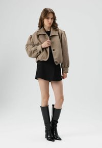 Brown cropped puffer jacket with an oversized collar and buttons, paired with a black mini dress and knee-high black heeled boots.