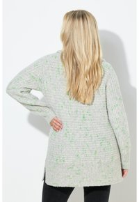 Jasnoszary sweter z dzianiny z zielonymi kropeczkami, o luźnym kroju, z długimi rękawami i ściągaczem na dole. Boczny rozcięcia dla większej swobody ruchów.