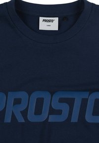 Granatowa bawełniana koszulka z dużym, kontrastowym nadrukiem "PROSTO" w kolorze niebieskim. Klasyczny krój z okrągłym dekoltem, miękka faktura i metka wskazująca rozmiar duży.