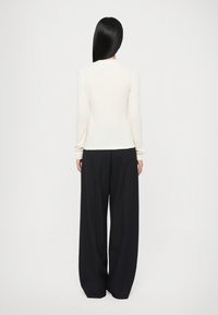 Pullover chiaro in crema con silhouette aderente e maniche lunghe, abbinato a pantaloni neri a gamba larga con texture a costine.