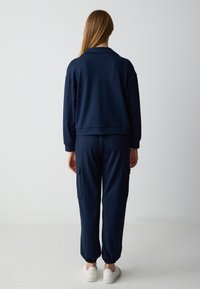 Tuta blu navy composto da una giacca corta con colletto e pantaloni cargo larghi con polsini elasticizzati, realizzati in un tessuto morbido e liscio.