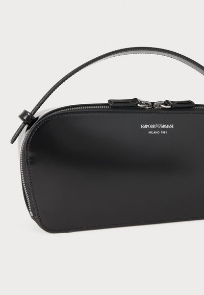 Sac à main noir Emporio Armani avec poignée supérieure incurvée, fermeture éclair argentée et texte de logo blanc sur surface en cuir lisse.