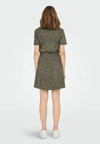 Grünes Leopardenmuster-Kleid mit kurzen Ärmeln, tailliertem Design und ausgestelltem Rock. Glattes Material mit subtiler Textur. Getragen mit weißen Sneakers.