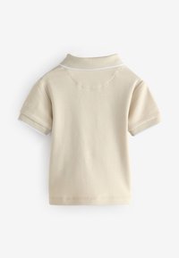 Beige kortärmad polo-tröja med krage, med vit sömnad vid kragen och ärmsluten. Enkel design, tillverkad av ett bomullsliknande material.