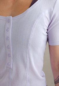 Haut lilas à manches courtes avec une texture côtelée, présentant un devant boutonné, un col rond et des coutures lisses pour un aspect ajusté.