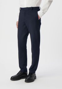 Granatowe spodnie w stylu tailored z elastycznym pasem, bocznymi kieszeniami i slim fit, połączone z czarnymi sznurowanymi butami.