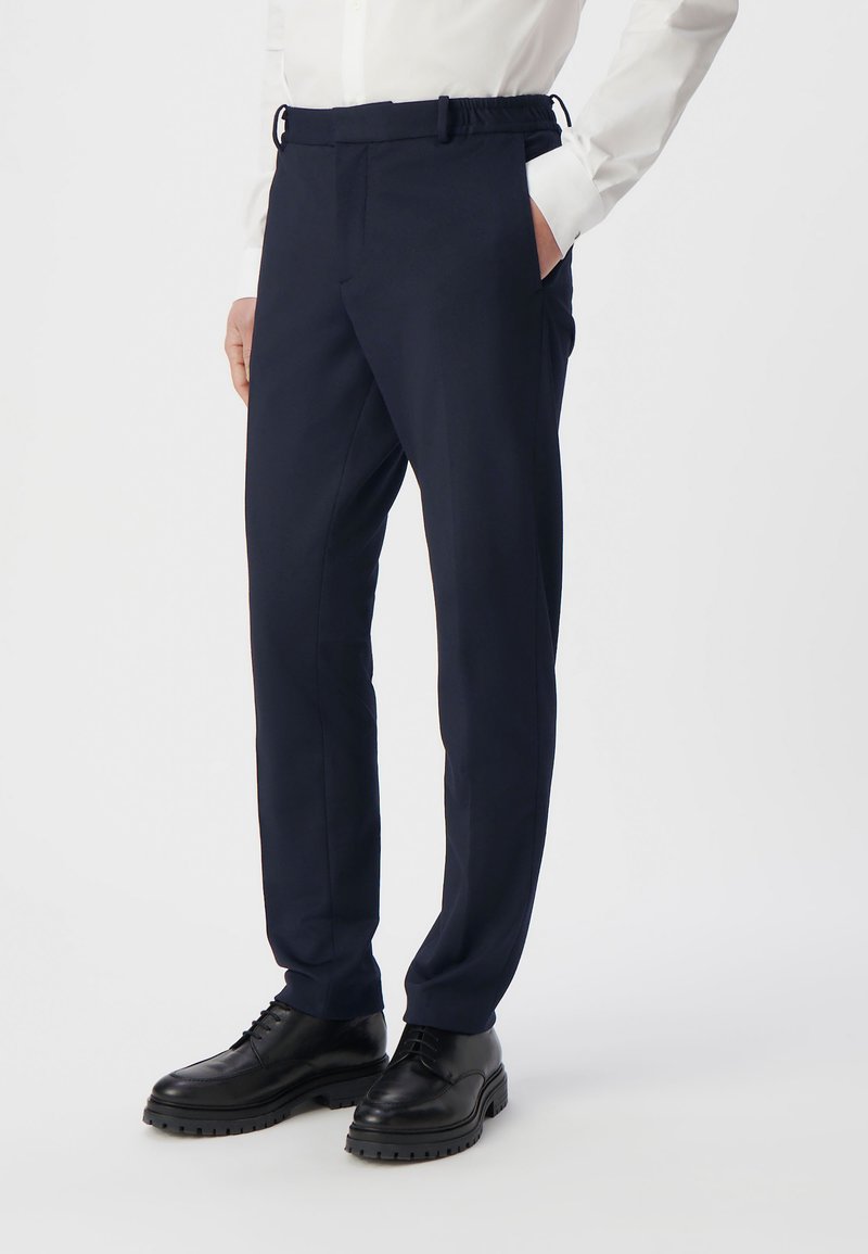 Granatowe spodnie w stylu tailored z elastycznym pasem, bocznymi kieszeniami i slim fit, połączone z czarnymi sznurowanymi butami.