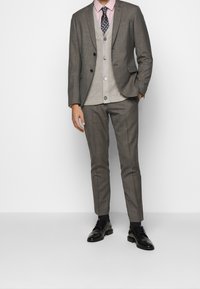 Completo grigio su misura con un finish effetto texture, abbinato a un gilet grigio chiaro, camicia rosa e cravatta a fantasia, completato da scarpe in pelle nere.