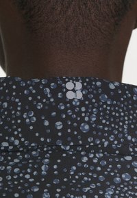 Černá látková košile s modrými a světle modrými kruhovými vzory. Význačný detail: malé logo ve světle šedé na límci.