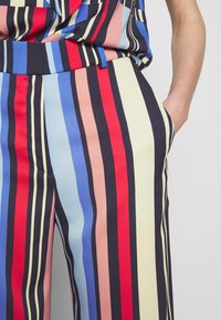 Pantalons en tissu rayé coloré rouge, bleu, rose et crème. Dotés d'une taille élastique et de poches sur les côtés. Texture lisse.