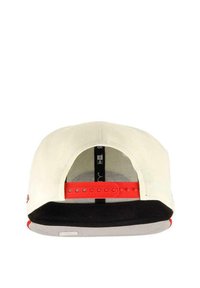 Snapback cap featuring a cream fabric body, red adjustable strap, black inner lining, and gray brim. Elements include ventilation mesh.