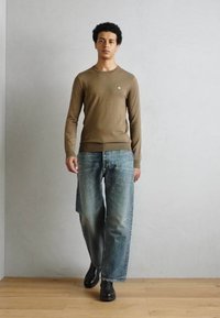 Bruine lange mouwen trui, lichtblauwe baggy jeans en zwarte schoenen. Eenvoudig ontwerp met ribbelmanchetten en - tailleband, schoenen met een glad accent.