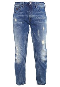 Jeans de mezclilla azul con un acabado desgastado, que presentan decoloración, marcas de uso y pequeños desgarros. Diseño clásico de cinco bolsillos, corte recto.