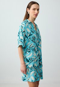 Abito a stampa floreale di colore teal, con maniche corte, colletto e vestibilità ampia. Il materiale sembra leggero con un motivo testurizzato.