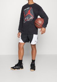 Svart långärmad tröja med röd och vit Chicago Bulls-logga, tillsammans med svarta och vita sportshorts och svarta joggingskor. Håller i en basketboll.