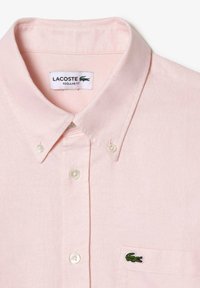 Camicia collare rosa chiaro con design a bottoni, caratterizzata da una sottile trama e logo del coccodrillo ricamato in verde sulla tasca del petto.
