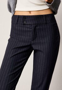 Marinblå randiga byxor med skräddarsydd passform, utrustade med två svarta knappar vid midjan och sidofickor för extra detaljer.