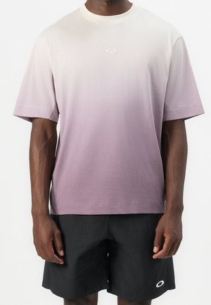 T-shirt à manches courtes dégradé du rose clair au violet, en coton, col rond, avec un petit logo sur la poitrine, porté avec un short noir.