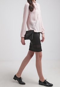 Blusa rosa chiaro con maniche lunghe e chiusura a bottoni, abbinata a una gonna nera aderente con pannelli trasparenti. Scarpe nere con lacci e una piccola borsa nera.