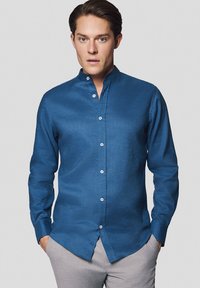 Niebieska koszula z długim rękawem, z kołnierzykiem stójkowym i gładką fakturą. Posiada białe guziki i dopasowany krój.