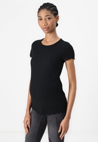 Top corto de manga corta negro con cuello redondo y bordes festoneados, combinado con jeans grises desgastados, presentado en un modelo.