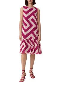 Ärmelloses, rosa und cremefarbenes Kleid mit Zickzackmustern und einem Rüschensaum. Kombiniert mit rosa Sandalen mit Riemchen.