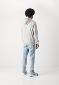 Grijze hoodie met een kangoeroezak, ribbel manchetten en zoom. Gecombineerd met lichtblauwe denim jeans en witte sneakers met grijze accenten.