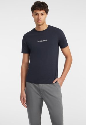Navyblaue Baumwoll-T-Shirt mit kurzen Ärmeln, mit dem weißen "GUESS JEANS"-Logo auf der Brust. Lässig geschnitten mit geradem Saum.