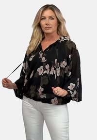 Czarna bluzka w kwiaty z długimi, szerokimi rękawami i luźnym krojem. Posiada kaptur i szczegóły ze sznurkiem, z kwiatowym wzorem w stonowanej różowej i zielonej kolorystyce.