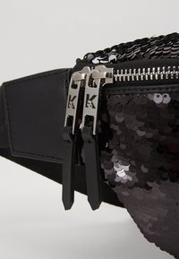 Marsupio nero con parte anteriore in paillettes, dotato di chiusura con zip e due cerniere in metallo argentato con logo. Texture liscia e finitura lucida.