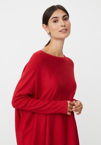 Červený oversized svetr s dlouhým rukávem, ribbovanou texturou, kulatým výstřihem a uvolněným střihem. Tkanina je jemná a lehká, což poskytuje dostatečnou splývavost.