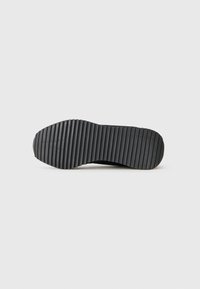 Black shoe sole with a ribbed tread pattern, displayed from the bottom on a plain white background.