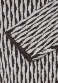 Tissu en laine douce avec des rayures verticales irrégulières noires et blanches et un coin plié montrant le même motif rayé.