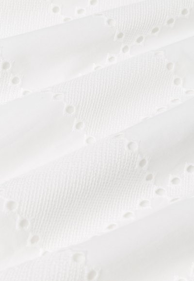 Tessuto bianco testurizzato caratterizzato da un motivo intrecciato e fori decorativi a occhio lungo i bordi, che offrono un dettaglio sottile e intricato.