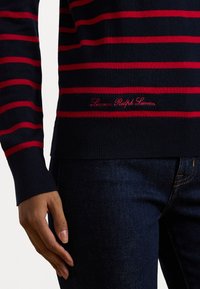 Mornarsko moder pulover z rdečimi vodoravnimi črtami, okrogla izrezanka, rebrasti manšeti in rob; vsebuje logotip "Lauren Ralph Lauren" v rdeči vezenini.