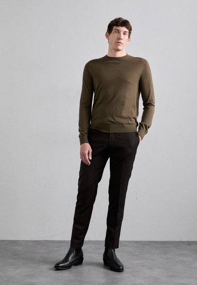 Olivenfarget tettsittende genser med lange ermer, rund hals, kombinert med mørkebrune skreddersydde bukser og svarte ankelstøvler. Enkelt, minimalistisk design.