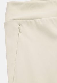 Close-up af beige bukser i stof med en lille skjult lynlås på den øvre sidesøm nær taljen.