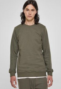Olijfgroene lange mouw sweatshirt met een ronde hals, ribgebreide manchetten en zoom. Zijdezachte textuur, eenvoudig ontwerp en minimale details.