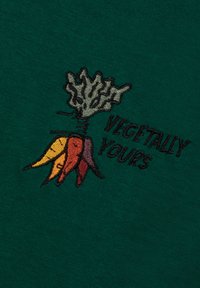 Borduurwerk van meerkleurige wortels met groene toppen naast de tekst "VEGETALLY YOURS" op donkergroene stof.