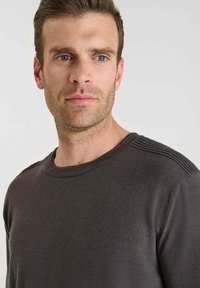 Gråstickad tröja med rundad halsringning, med ribbade detaljer på axlarna och en slät yta.