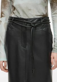 Crna kožna suknja s remenom na vezanje, s glatkom teksturom i suptilnim detaljima šivanja. Uparena s laganom, uzorkovanom majicom dugih rukava.