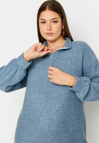 Pullover in pile azzurro chiaro, con mezza zip e collo alla coreana, e maniche a sbuffo. Il tessuto strutturato evidenzia un aspetto morbido e accogliente.